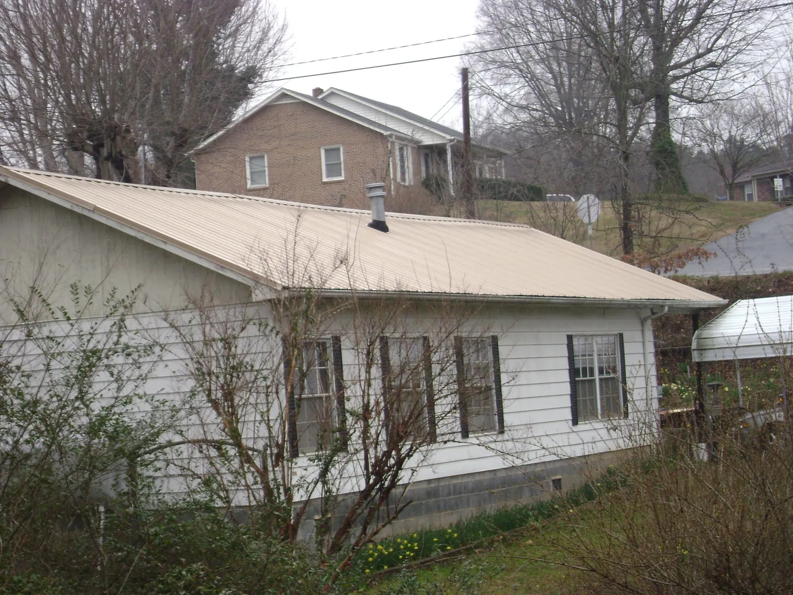 Tan metal roof on a white sided house set into a hillside — Commercial Roofing by Roofing Brothers in Hume